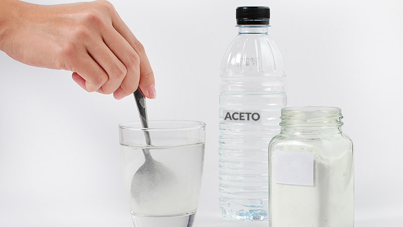 mano mescola liquido in un bicchiere con a fianco bottiglia con scritta aceto e altro contenitore in vetro